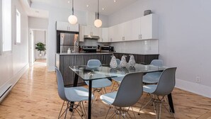 A modern kitchen with white cabinets, stainless steel appliances, and a glass dining table with four chairs. - Welcoming and Homey unit near Mount Royal by DenStays (Montréal)