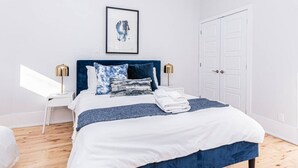 A neatly made bed with a blue headboard, white bedding, and a folded towel on the side. - Welcoming and Homey unit near Mount Royal by DenStays (Montréal)