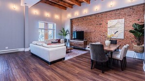 A spacious living room with a white sofa, a dining table, and a brick wall.