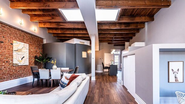 A modern interior with exposed wooden beams, a brick wall, and a dining area with white furniture.