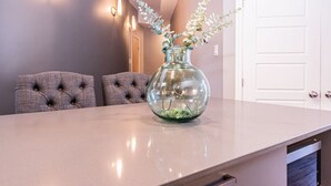 A modern kitchen with a marble countertop, a glass vase with greenery, and a white door in the background.