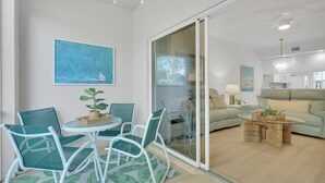 Ein modernes Wohnzimmer mit einem Glastisch, grünen Sesseln, einem Sofa und einem Essbereich mit weißem Tisch und Stühlen.