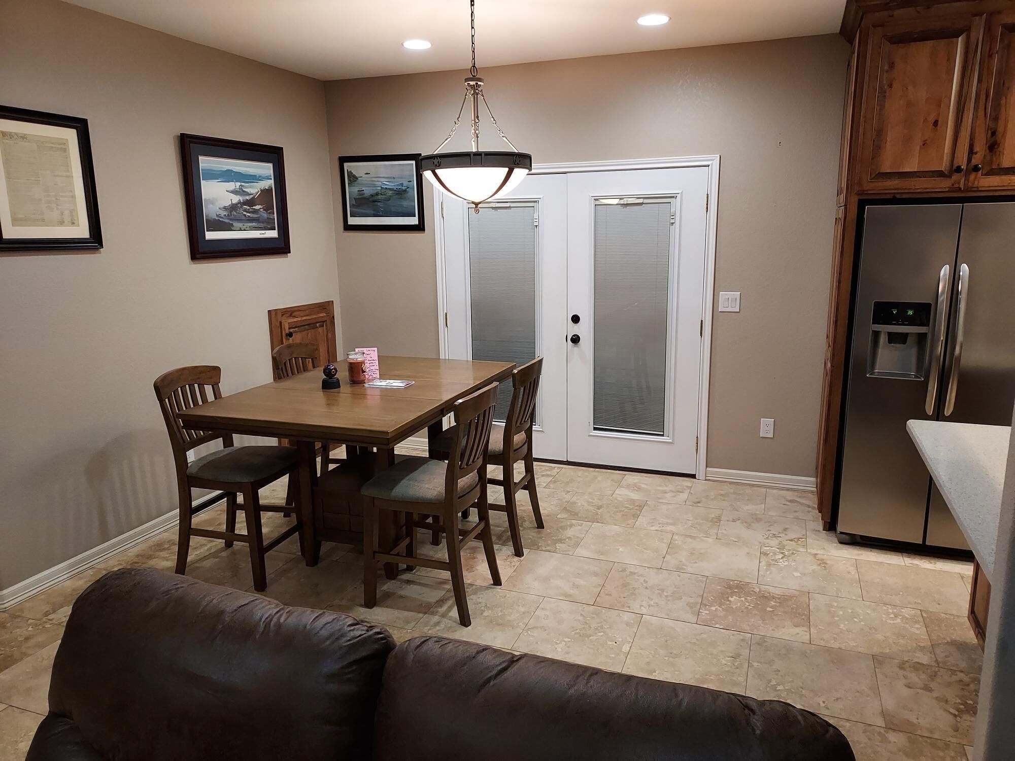 A dining area with a wooden table and chairs, a chandelier, a refrigerator with a water dispenser, and a door with frosted glass panels.