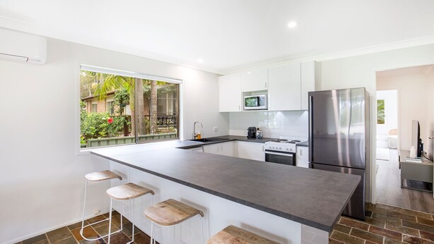 A modern kitchen with a large island, white cabinetry, stainless steel appliances, and a view of a garden. - Hanalei - Pet Friendly - Directly Opposite Waterfront (Myola)