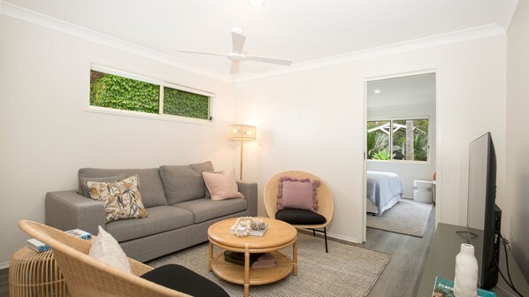 A modern living room with a grey sofa, a round wooden coffee table, a wicker chair, and a floor lamp. - Hanalei - Pet Friendly - Directly Opposite Waterfront (Myola)