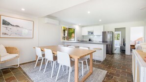 A modern kitchen with white cabinetry, a stainless steel refrigerator, and a dining area with a wooden table and white chairs. - Hanalei - Pet Friendly - Directly Opposite Waterfront (Myola)