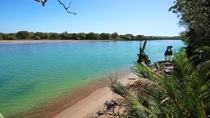 A clear view of a beach with calm water, sandy shore, and dense greenery. - Hanalei - Pet Friendly - Directly Opposite Waterfront (Myola)