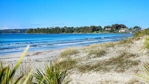 A beach with clear blue water, sandy shore, and some vegetation in the foreground. - Hanalei - Pet Friendly - Directly Opposite Waterfront (Myola)