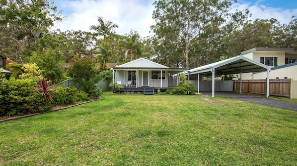 A residential property with a covered patio, a lawn, and a variety of trees and shrubs.