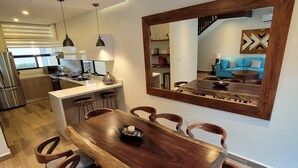Een moderne eetruimte met een houten tafel en stoelen, een keuken op de achtergrond en een grote spiegel aan de muur.