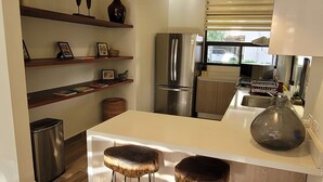 Een moderne keuken met een centraal eiland, roestvrijstalen apparatuur, hangende lampen en houten planken.