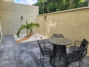 A patio with a round table and six chairs, surrounded by a low stone wall and a palm tree. - Dream  Home in playa del carmen (Playa del Carmen)
