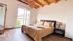Een slaapkamer met een houten plafond, een bed met beige beddengoed, twee nachtkastjes met lampen, en een glazen schuifdeur naar een balkon.