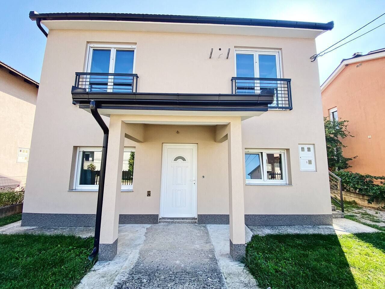 Un edificio a due piani con un ingresso centrale, un balcone al piano superiore e un piccolo portico.