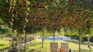 Een buiten eethoek met een tafel voor twee personen, een zwembad op de achtergrond en een pergola erboven.