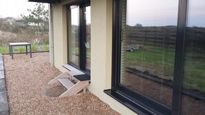 A patio with a wooden bench and a table, large windows offering a view of a grassy field and a fence. - Impeccable Studio in Ouddorp 400m from th (Ouddorp)