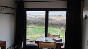 A room with a table and chairs facing a large window with a view of a grassy field and hills. - Impeccable Studio in Ouddorp 400m from th (Ouddorp)