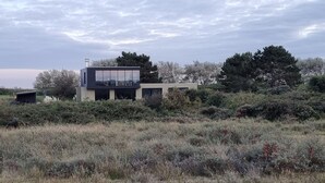 A modern house with a large glass facade, surrounded by dense shrubbery and trees. - Impeccable Studio in Ouddorp 400m from th (Ouddorp)