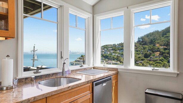 A kitchen with two large windows, a stainless steel sink, a dishwasher, and wooden cabinets.