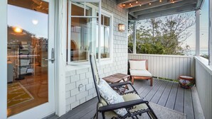 A covered deck with a wooden floor, a chair, a small table, and string lights.