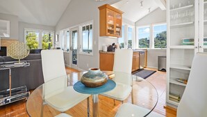 A modern kitchen with white cabinetry, a dining area with a glass table, and a view of the outdoors.