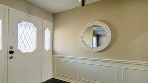 A hallway with a white door, a round mirror on the wall, and a light fixture above. - THE BRIAR Beautiful spacious home in quiet neighborhood. Close to dining and shopping! Broadway Ave. (Tyler)
