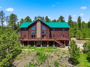 A two-story log cabin with a green roof, multiple balconies, and a stone chimney.