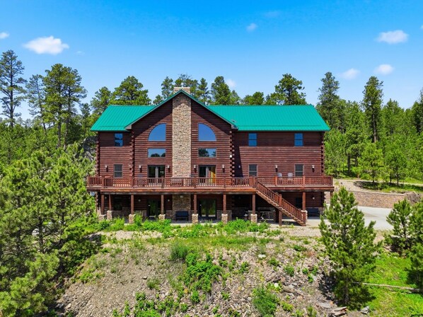 A two-story log cabin with a green roof, multiple balconies, and a stone chimney.