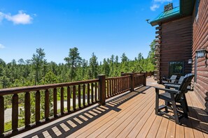 A wooden deck with a railing, outdoor seating, and a view of a forest.