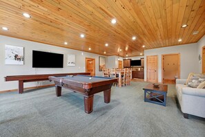 A spacious room with a pool table, a television mounted on the wall, and a seating area with a sofa and chairs.