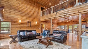 A log cabin interior with a living room featuring two leather sofas, a coffee table, and a large window.