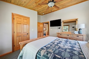 A bedroom with a bed, wooden wardrobe, a television, and a ceiling fan.