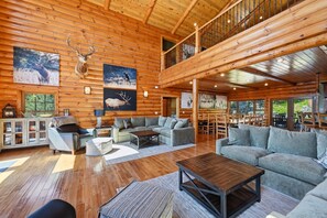 A spacious log cabin interior with a loft, wooden floors, and a dining area.