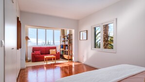Ein geräumiges Zimmer mit einem großen Bett, einem roten Sofa, einem hölzernen Bücherregal und einem großen Fenster mit Aussicht.