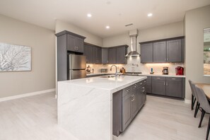 A modern kitchen with dark cabinets, a marble island, and stainless steel appliances. - Stunning 3 bedroom with Pool/Hot Tub/Game Room (Escondido)