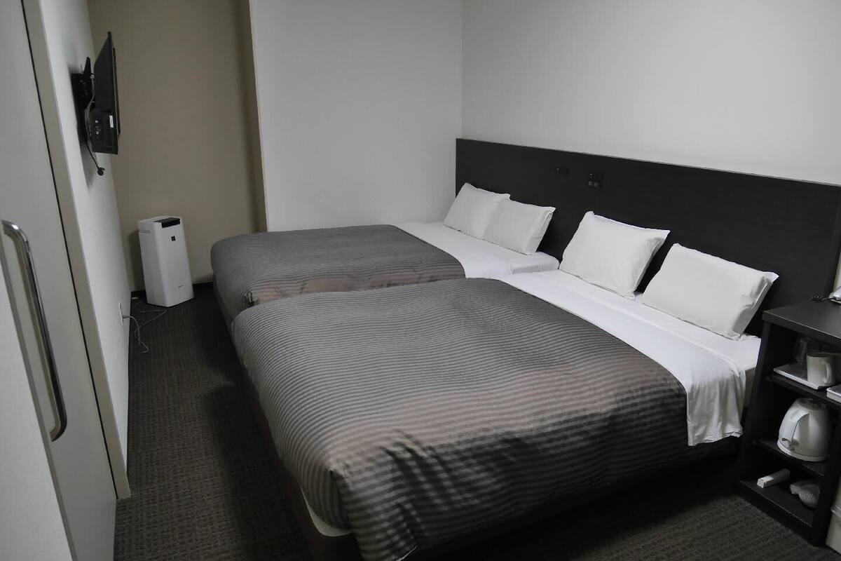 Quarto de hotel com duas camas, uma mesa de cabeceira, um abajur e uma pequena estante com uma chaleira.