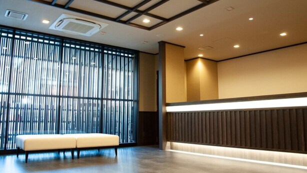 A modern interior with a seating area, a large window with vertical blinds, and a recessed ceiling with lighting. - HOTEL GLANY's KOSHIGAYA premier (Koshigaya)