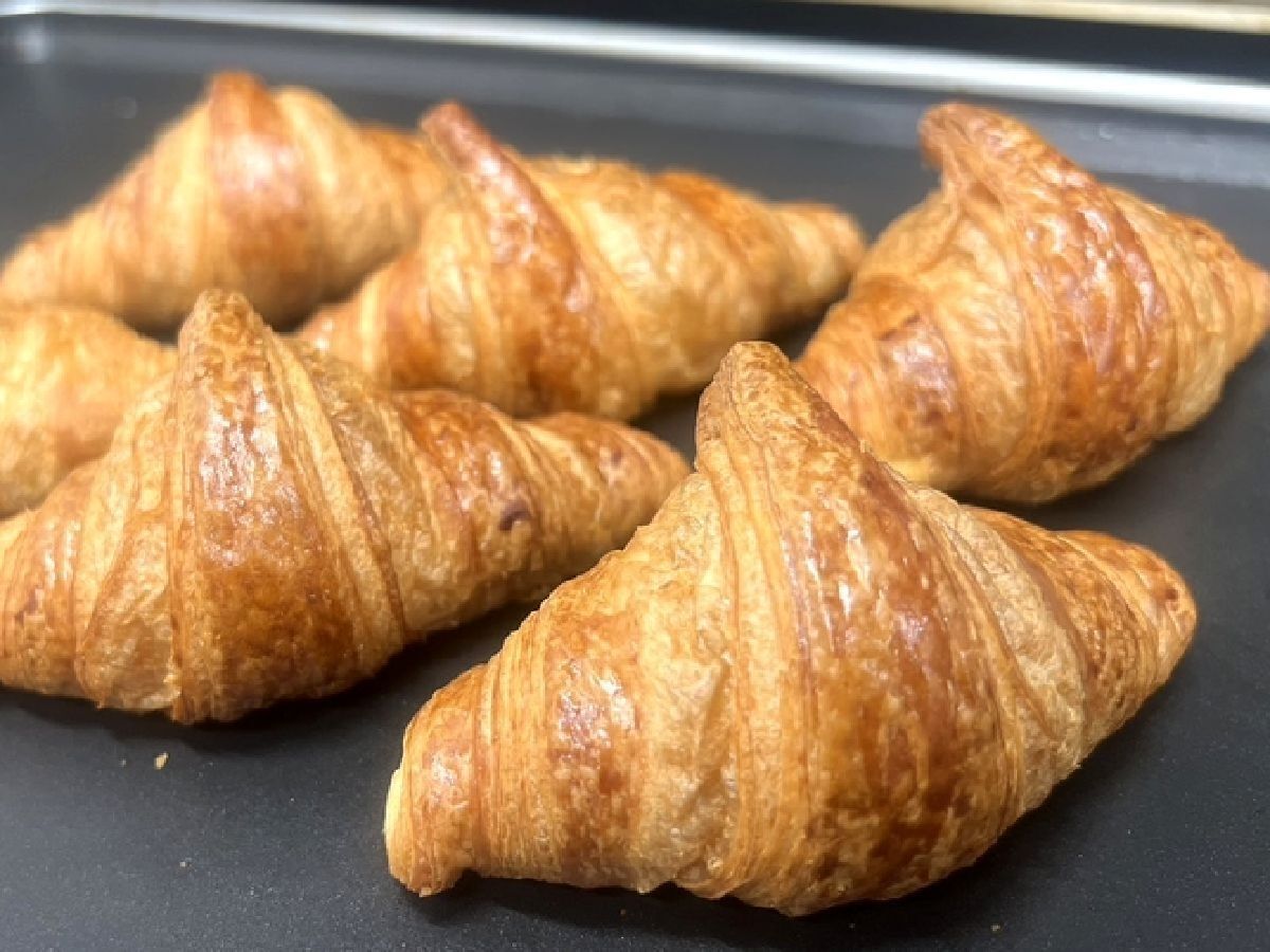 Four golden-brown croissants on a black tray.