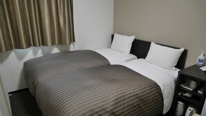 A hotel room with a double bed, a bedside table with a bottle of hand sanitizer, and a small shelf with a kettle and other items. - HOTEL GLANY's KOSHIGAYA premier (Koshigaya)
