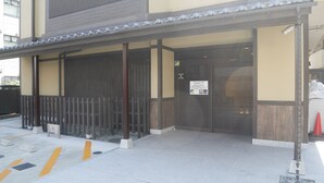 A building entrance with a traditional wooden gate, a signboard, and a tiled pavement with directional arrows. - HOTEL GLANY's KOSHIGAYA premier (Koshigaya)