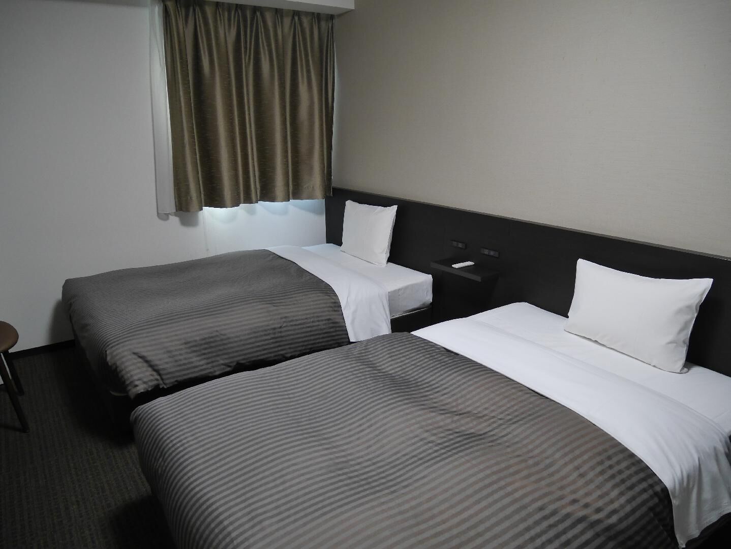 A hotel room with two beds, a nightstand, a chair, and a window with curtains.