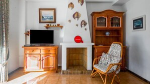 A living room with a television, a fireplace, a wooden cabinet, and a wicker chair. - Rinconada Real by Interhome (Benidorm)
