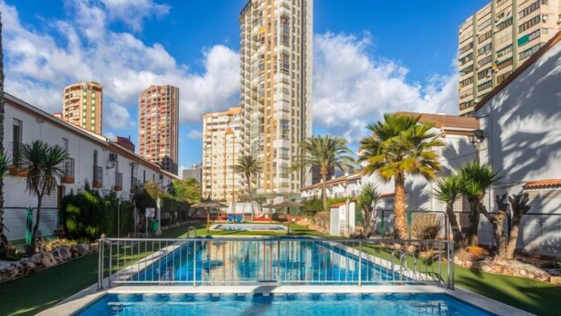 A swimming pool surrounded by greenery, with tall residential buildings in the background. - Rinconada Real by Interhome (Benidorm)