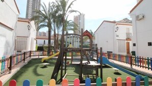 A playground with slides and climbing structures, surrounded by white buildings and palm trees. - Rinconada Real by Interhome (Benidorm)