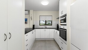 A modern kitchen with white cabinets, a black countertop, a window, and a built-in oven.