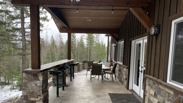 A covered outdoor patio with stone walls, a wooden table, and chairs. - Entire guesthouse, quiet wooded area of Cocolalla (Cocolalla)