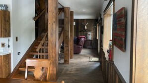 A wooden staircase leading to a second floor, a dining area with a wooden table and chairs, and a living room with a sofa and a decorative wall piece. - Entire guesthouse, quiet wooded area of Cocolalla (Cocolalla)