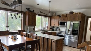 A modern kitchen with wooden cabinets, a central island, stainless steel appliances, and a dining area with a wooden table and chairs. - Entire guesthouse, quiet wooded area of Cocolalla (Cocolalla)