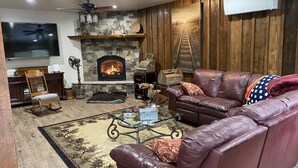 A cozy living room with a stone fireplace, leather sofa, and a flat-screen TV. - Entire guesthouse, quiet wooded area of Cocolalla (Cocolalla)