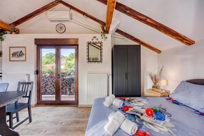 A bedroom with a bed, a desk, a chair, a wardrobe, and a view through a door.